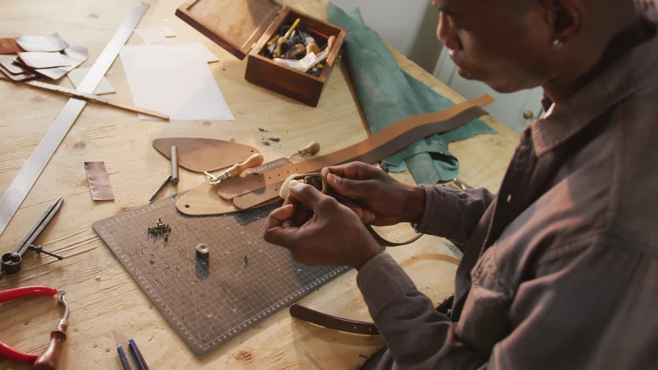 artesano afroamericano enfocado usando herramientas para hacer un cinturón en un taller de cuero