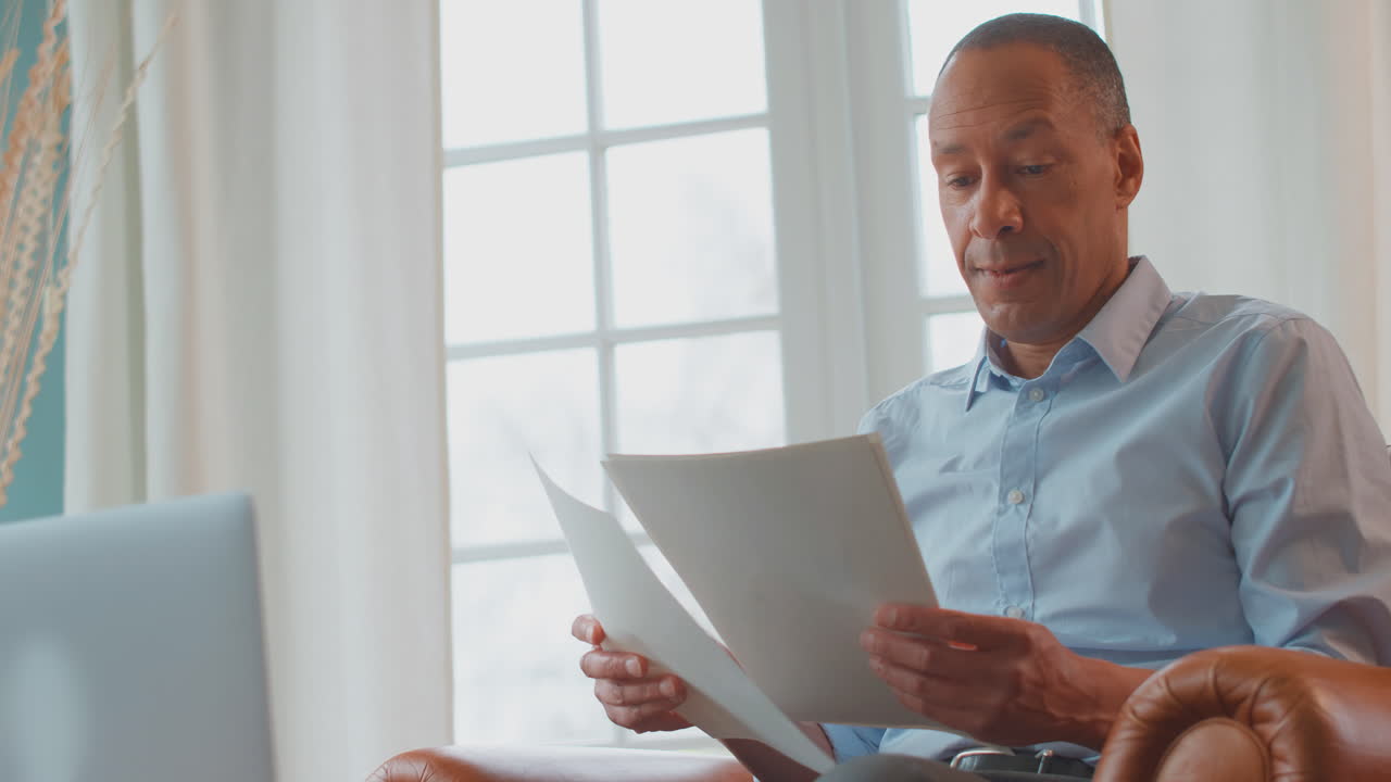 Mature Man Or Businessman Working From Home Sitting In Armchair Looking Through Paperwork