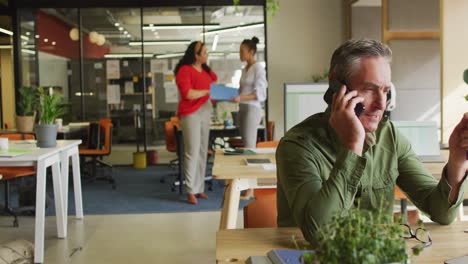 happy caucasian businessman sitting at table and using smartphone at office