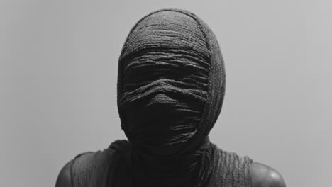 a mummy of a woman on a white backdrop rises her head