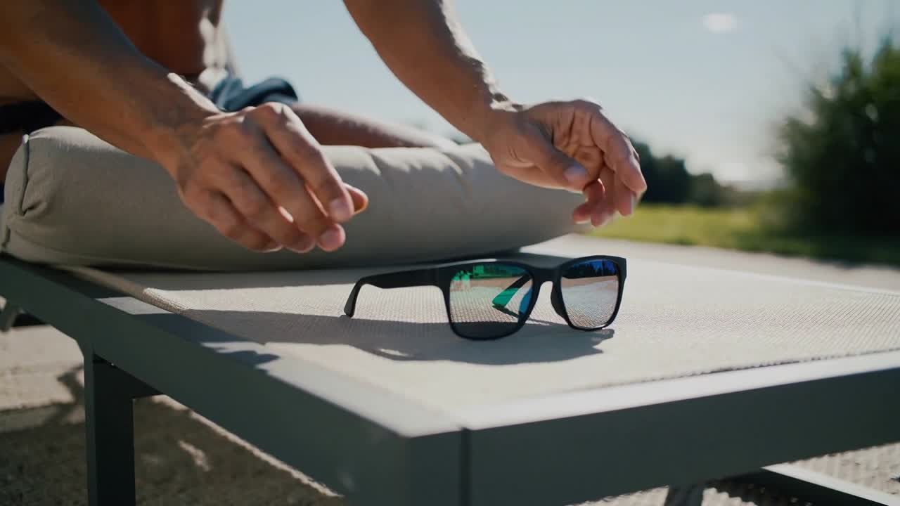Reaching shirtless man picking up aligning placing mirrored shades on patio table to rest
