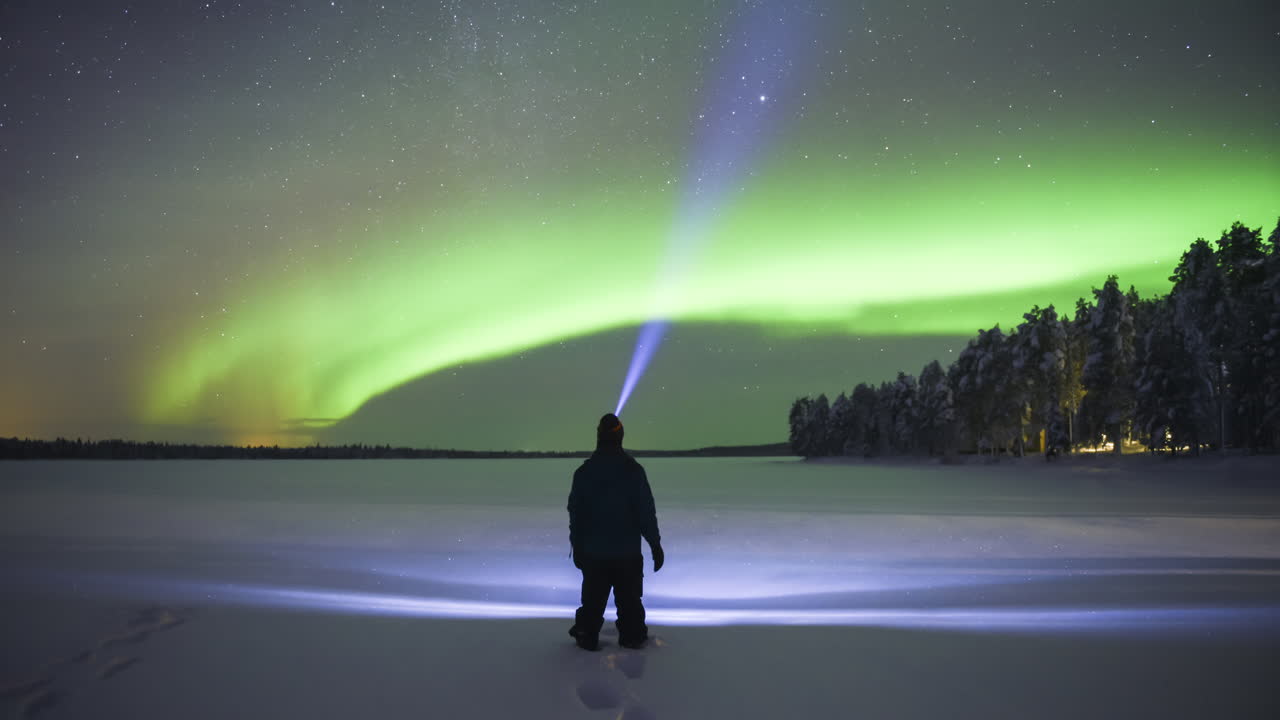 Timelapse of person watching aurora borealis during strong bright green northern lights display in unique amazing travel experience. Time lapse in Lapland, Finland