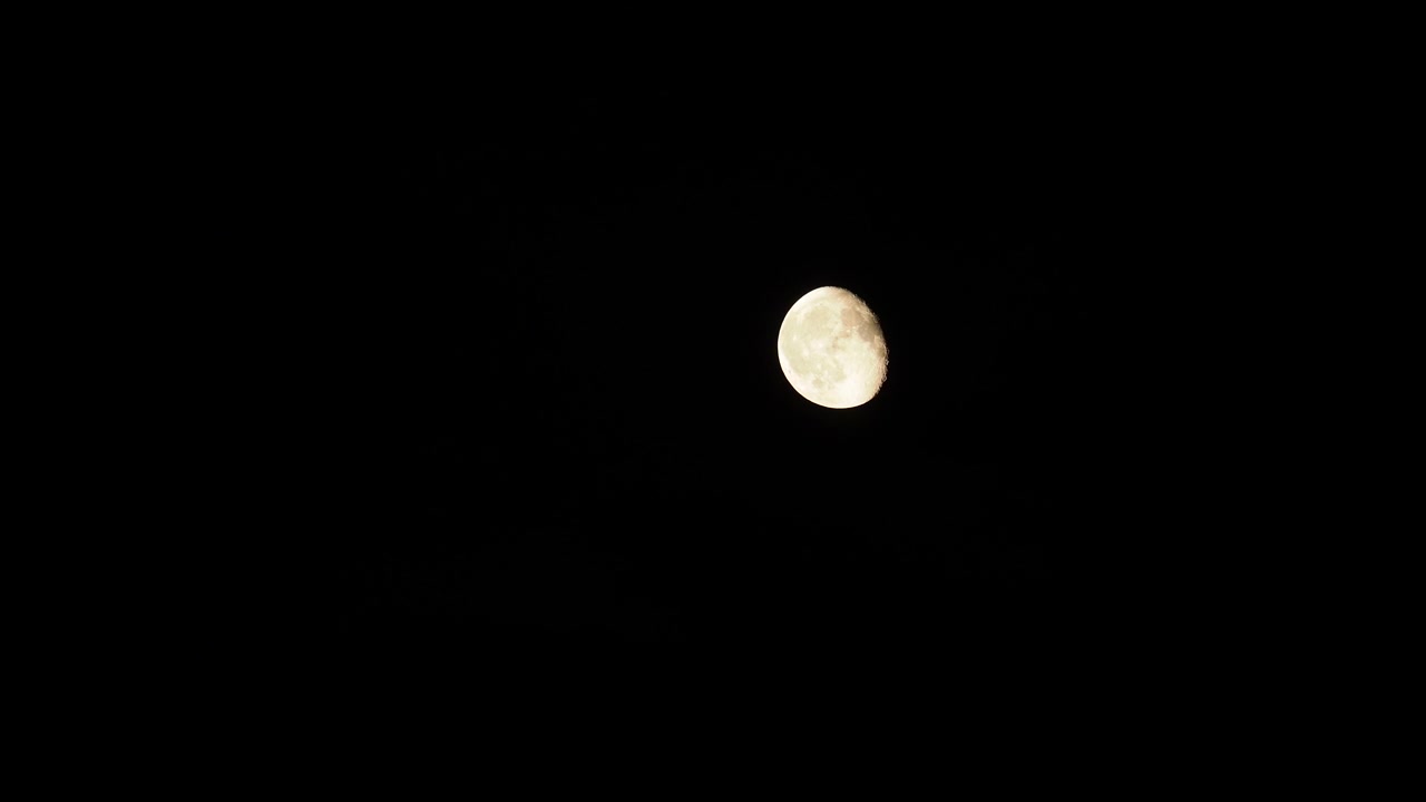 Lua Cheia surge por trás das nuvens no céu noturno escuro.