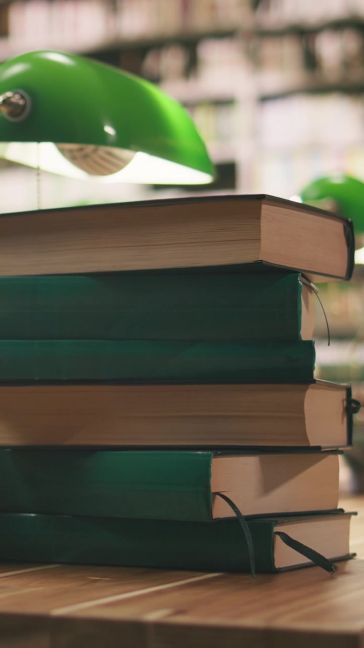 Vertical Video Stack of green hardcover books in library desk scene with blurred bookshelves