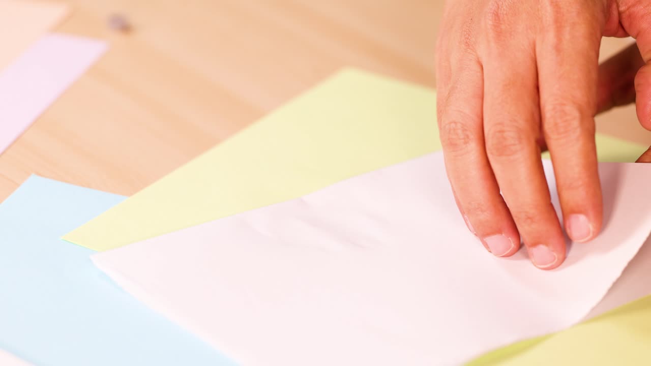 Hands press and reveal vibrant acrylic paint pattern on white paper, bright tabletop, overhead view