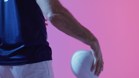 caucasian male rugby player with rugby ball over pink lighting