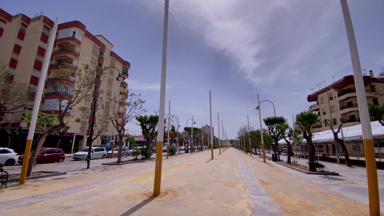 Paseo urbano con árboles y edificios en un pueblo costero español, ofreciendo un ambiente sereno para caminar y andar en bicicleta.