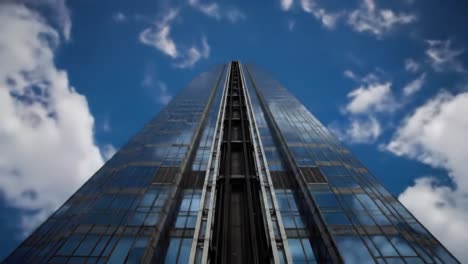 a tall skyscraper stands majestically against a blue sky dotted with clouds. the glass facade reflects light and adds to the cityscape's modern charm.