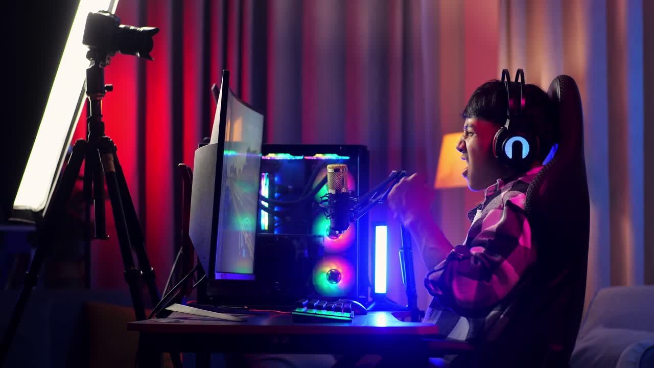 vista lateral de un niño asiático que grita gol y baila celebrando el juego ganador a través de la red en una computadora personal. videojuego de transmisión en vivo, escritorio iluminado por luz de tira led rgb