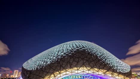 futuristic dome glowing vibrantly at night beneath a dramatic cloud filled sky, offering a captivating display of modern architecture and innovative design in an urban landscape