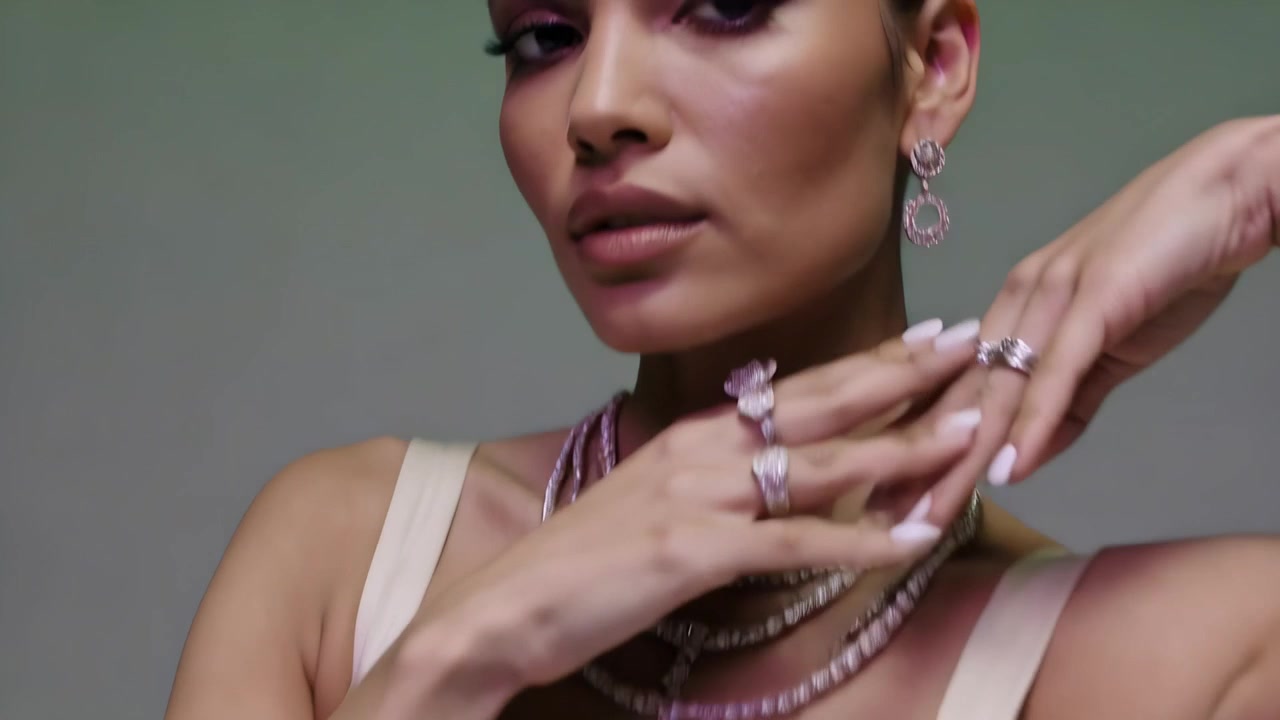 Modella che inizia una piroetta, facendo perno su tacchi argentati sul pavimento dello studio, mentre mostra un abito color crema e gioielli.