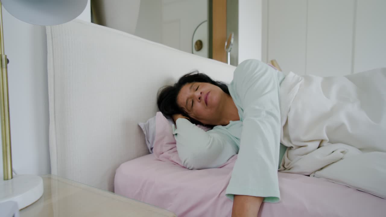 Alarm ringing African American woman waking in bed, muting alarm with ringed hand, partner stirring