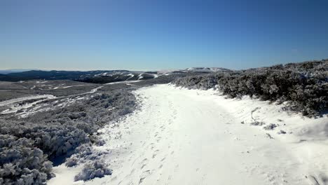 Aerial-shot-flying-over-a-snowy-area-on-a-mountain-and-the-horizon-with-mountains-in-the-background-in-Manzaneda,-Galicia