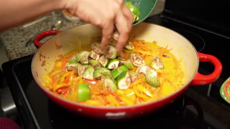 hands of chef putting raw brinjals on frying pan with sliced bell paper. veg recipe.