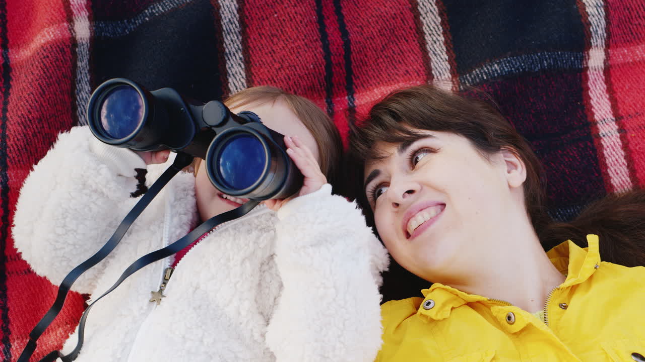 어린 소녀를 둔 젊은 여성은 등에 등을 대고 하늘에서 쌍안경을 들여다본다