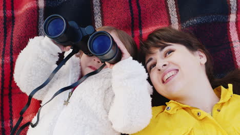 young woman with a little girl lie on her back and look through binoculars in the sky