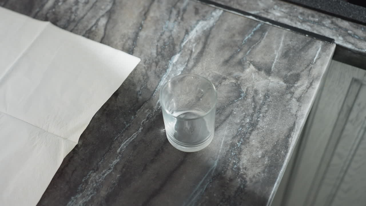 Top down view of woman with manicured nails carefully arranging glass cups on marble countertop with open tissue paper nearby, showcasing neatness