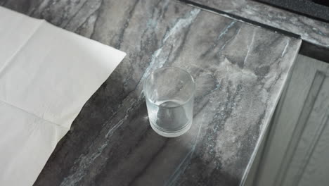 top down view of woman with manicured nails carefully arranging glass cups on marble countertop with open tissue paper nearby, showcasing neatness