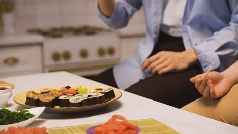 hombre japonés recogiendo un trozo de sushi con palillos y dándoselo a su amigo para que lo pruebe