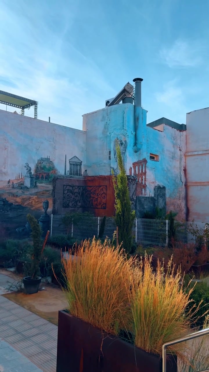 Alicante, Spagna, 8 agosto 2025: Cortile urbano moderno con piante in vaso e un murale di rovine romane