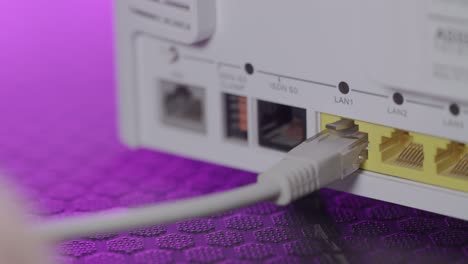 primer plano de un hombre instalando un cable de conexión de red ethernet en un enrutador con una luz colorida en el fondo