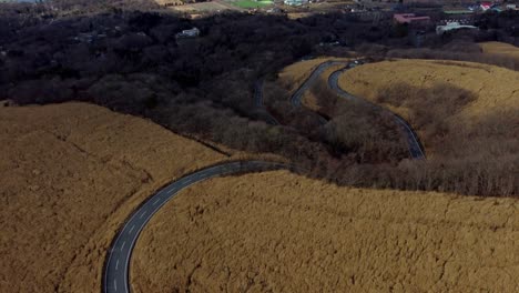 Curvy-road-winding-through-golden-brown-hills,-aerial-view,-late-afternoon-light