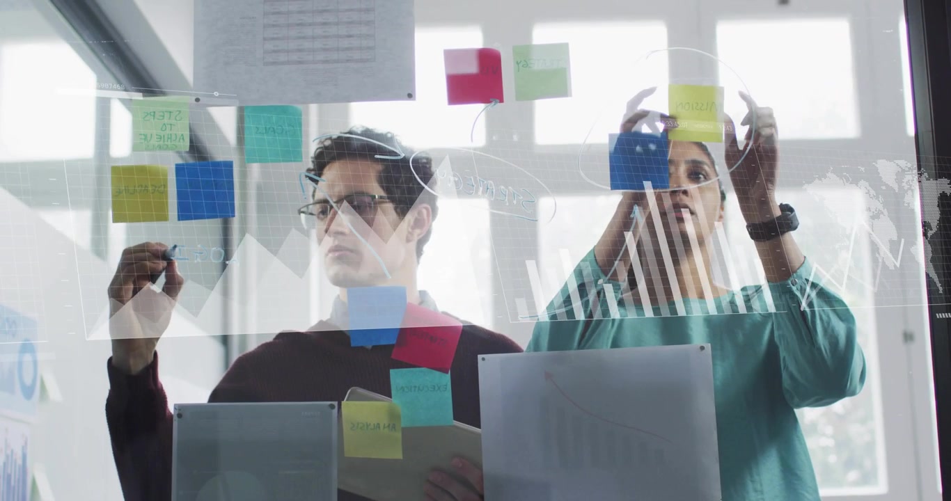 Right reaching to place top sticky note, left sketching connectors on glass, organizing team ideas