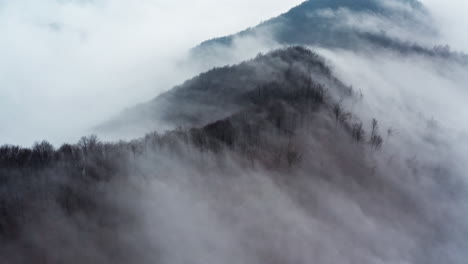 Neblige-Berge-Mit-Kahlen-Bäumen,-Eingehüllt-In-Dichten-Nebel,-Der-Eine-Heitere,-Geheimnisvolle-Atmosphäre-Hervorruft