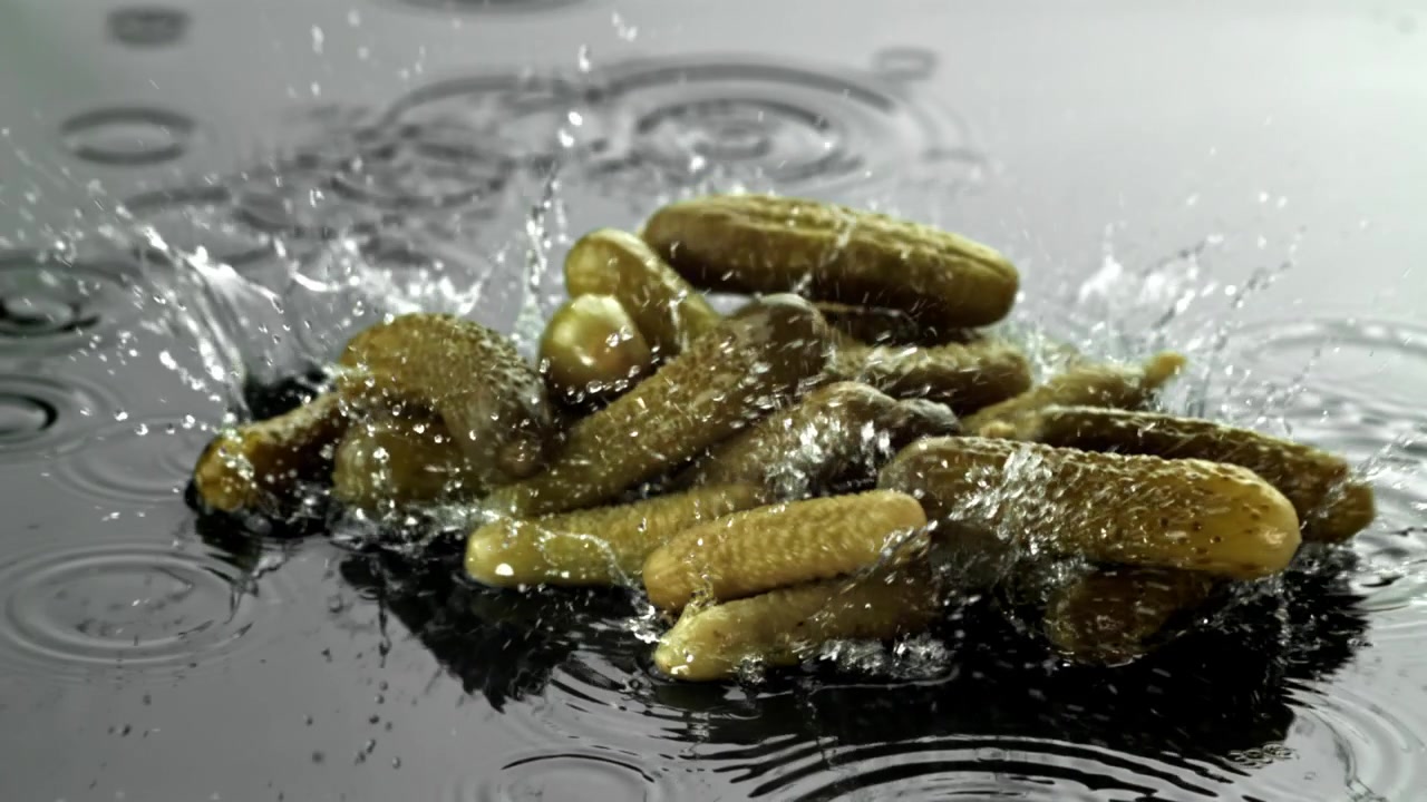 Cetriolini sottaceto che cadono nell'acqua con schizzi al rallentatore