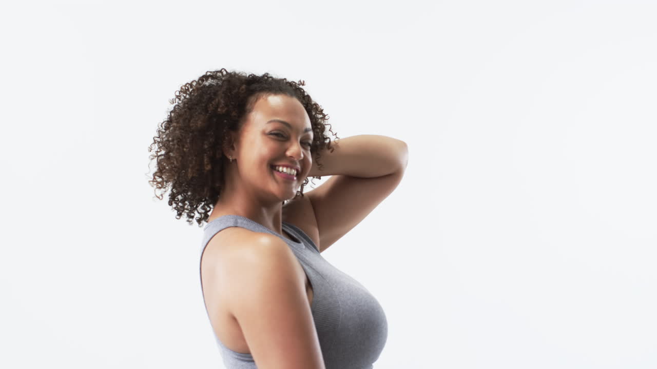 Young biracial plus size woman with curly hair smiling and posing in studio, copy space