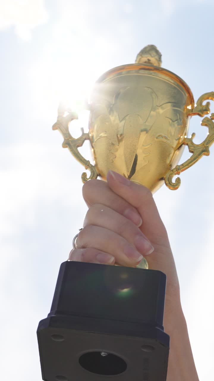 Mano che tiene un trofeo d'oro in primo piano con sfondo di cielo esterno. Concetto di realizzazione, successo, vittoria, motivazione, riconoscimento e celebrazione della vittoria.