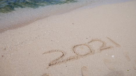 the writing 2021 on the white sand of the beach is lost by the waves