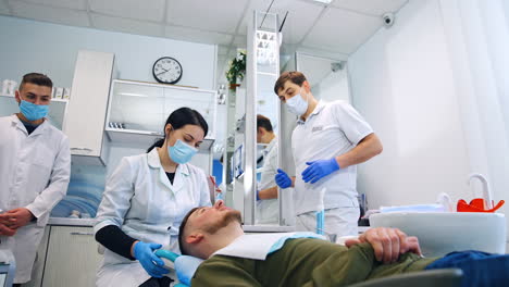 teacher is showing the students the work of a dentist. female students sits behind the patient lying on chair. low angle view.