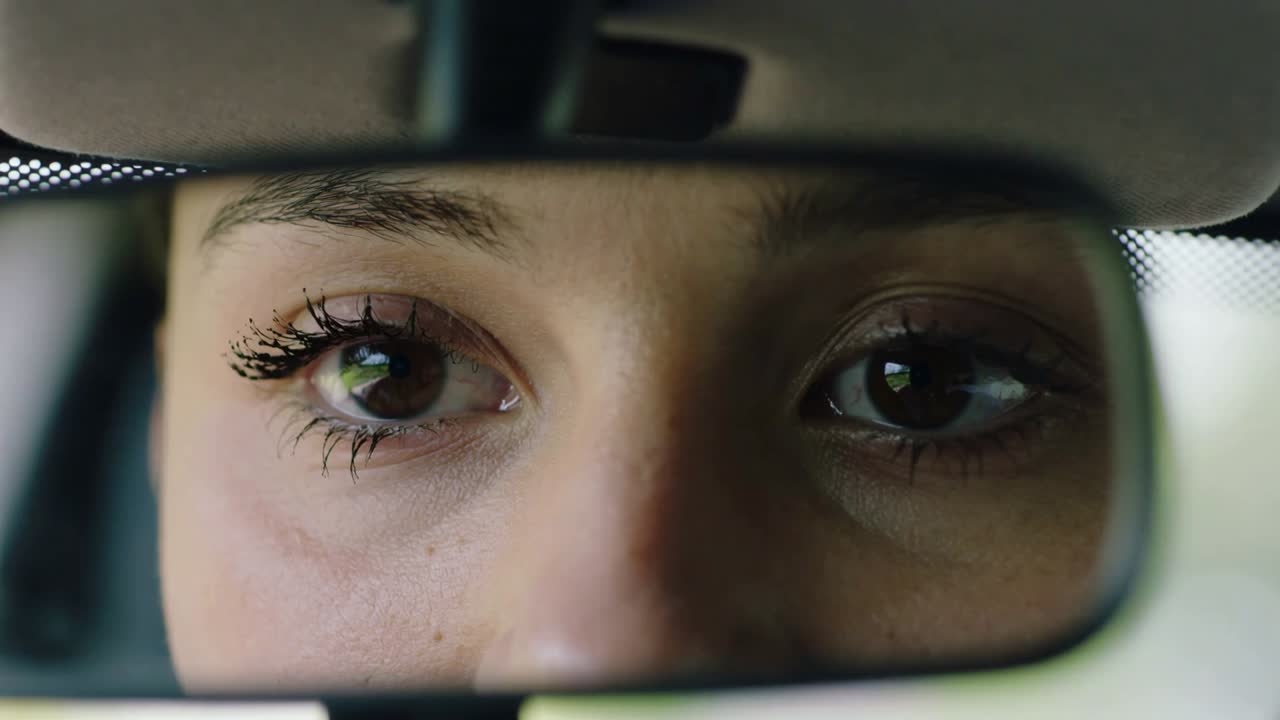 Checking rearview mirror, Hispanic woman shifting gaze left and right inside car, mascara visible