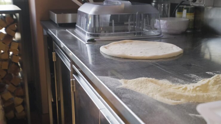 Primo piano di farina e impasto per pizza su un piano di lavoro in una cucina di ristorante