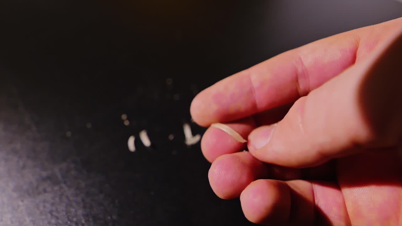 Unusual close up male fingers twist freshly cut toenail piece in low light