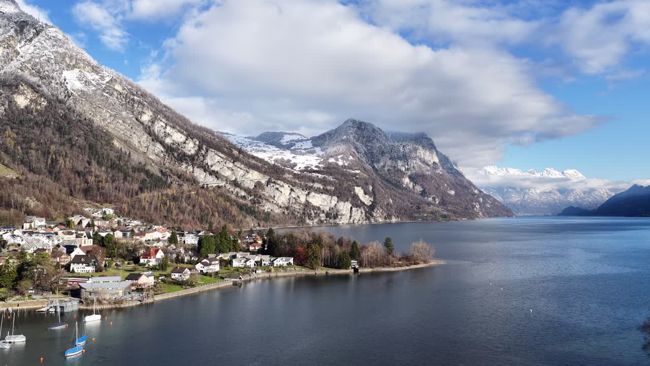 Walensee Switzerland with lakeside village, blue water and snowy mountains as drone orbits forward, peaceful alpine landscape