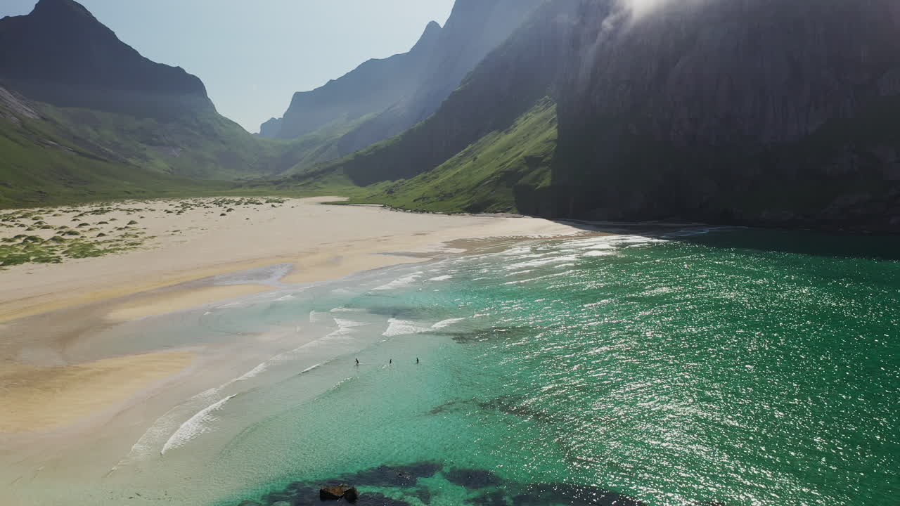 Large plan cinématographique au drone révélant trois personnes nageant à la plage de Horseid dans une eau bleu turquoise