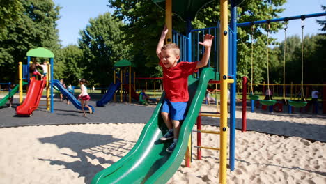 a happy boy plays on a slide at a busy outdoor playground