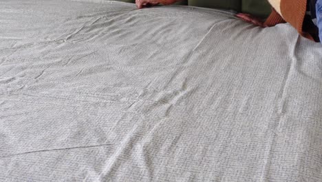 a person making a bed with a white patterned bed sheet.