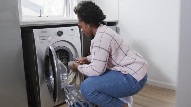 African american woman putting clothes into washing machine, doing laundry at home, slow motion
