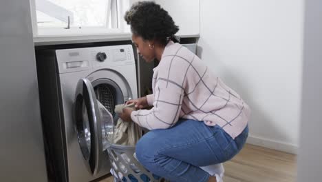 Mujer-Afroamericana-Poniendo-Ropa-En-La-Lavadora,-Lavando-Ropa-En-Casa,-Cámara-Lenta