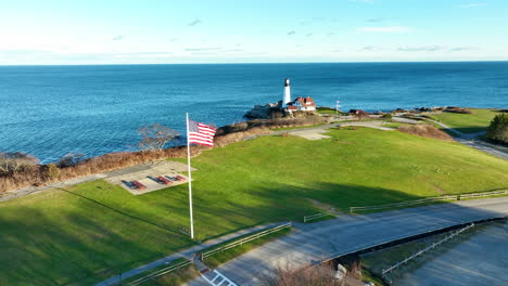 national flag of the united states of america gently flutters in the wind with in the background the historical portland head light house on a sunny day