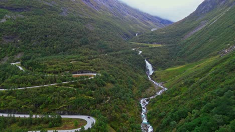 Aerial-along-a-winding-road-next-to-a-stream-near-Hjelledalen,-Norway