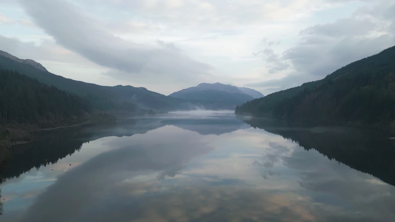 A long, calm lake reflecting the forested peaks, Aerial RIse