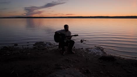 silhouette of a musician playing guitar at sunset by the lake