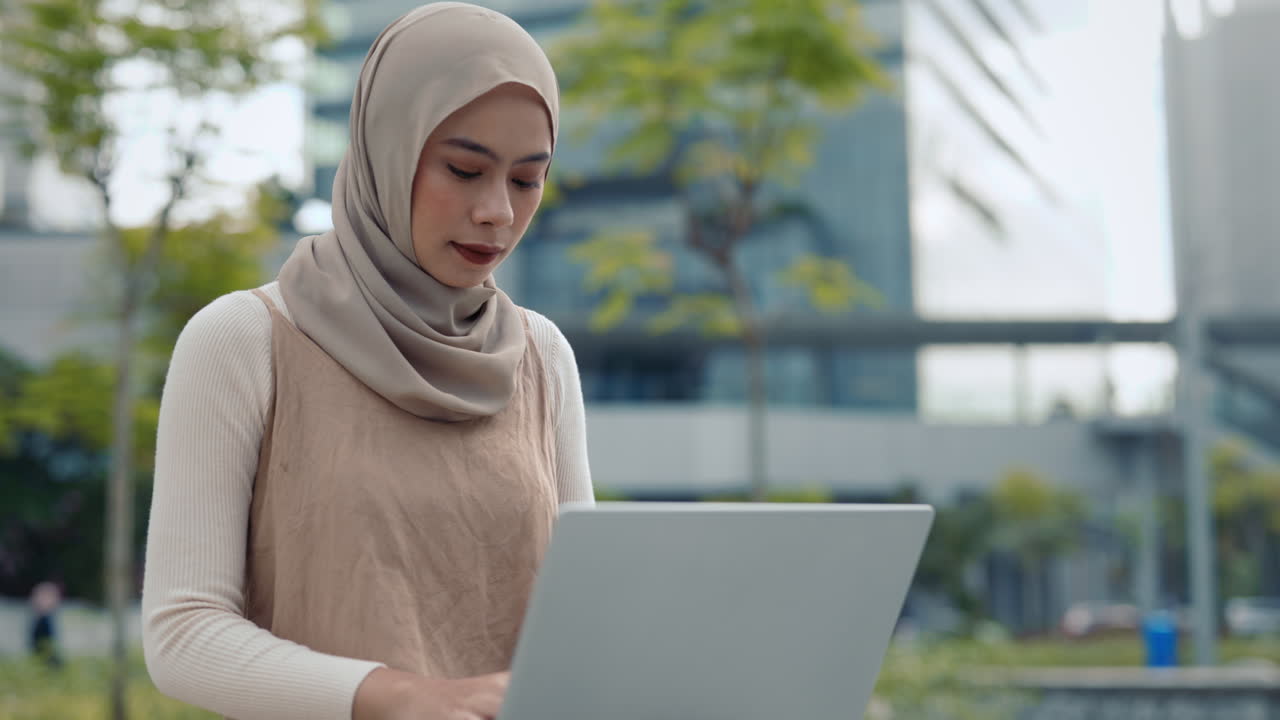 Woman in hijab using laptop outdoors | Premium Stock Video Footage