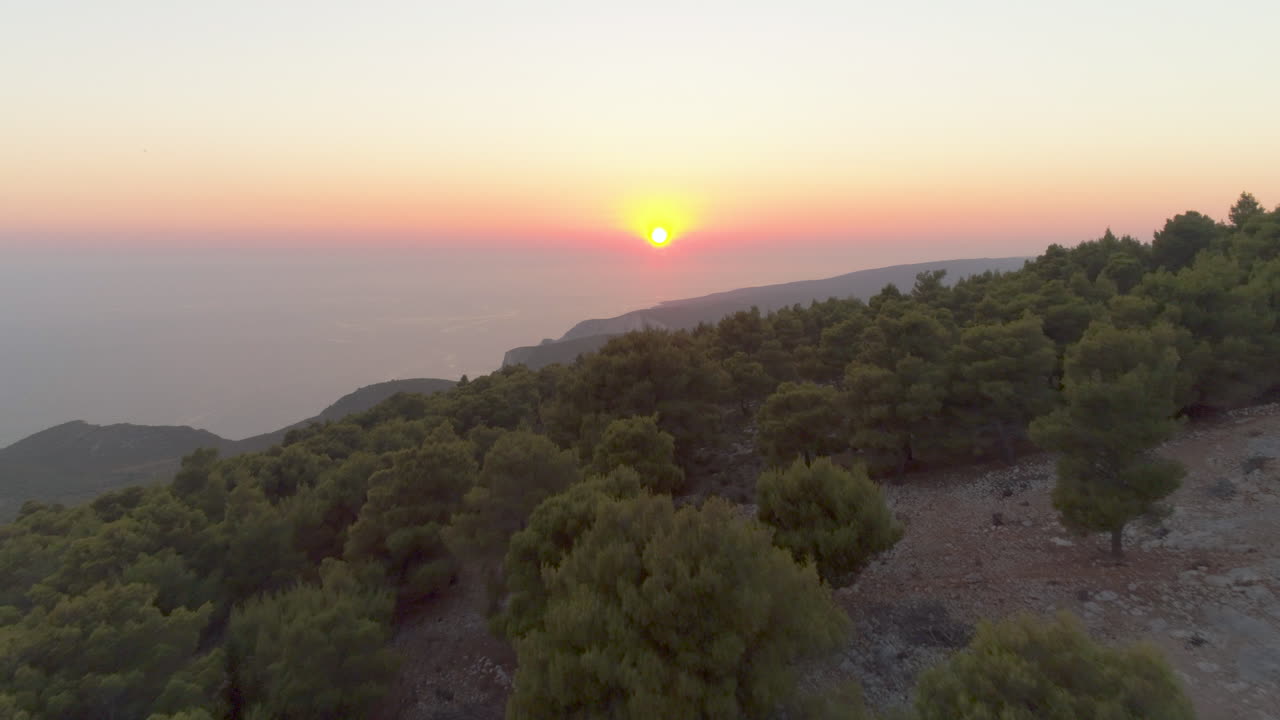 Vista aérea sobre a paisagem florestal da ilha grega de Zakynthos, em direção a um horizonte nebuloso e colorido ao pôr do sol.