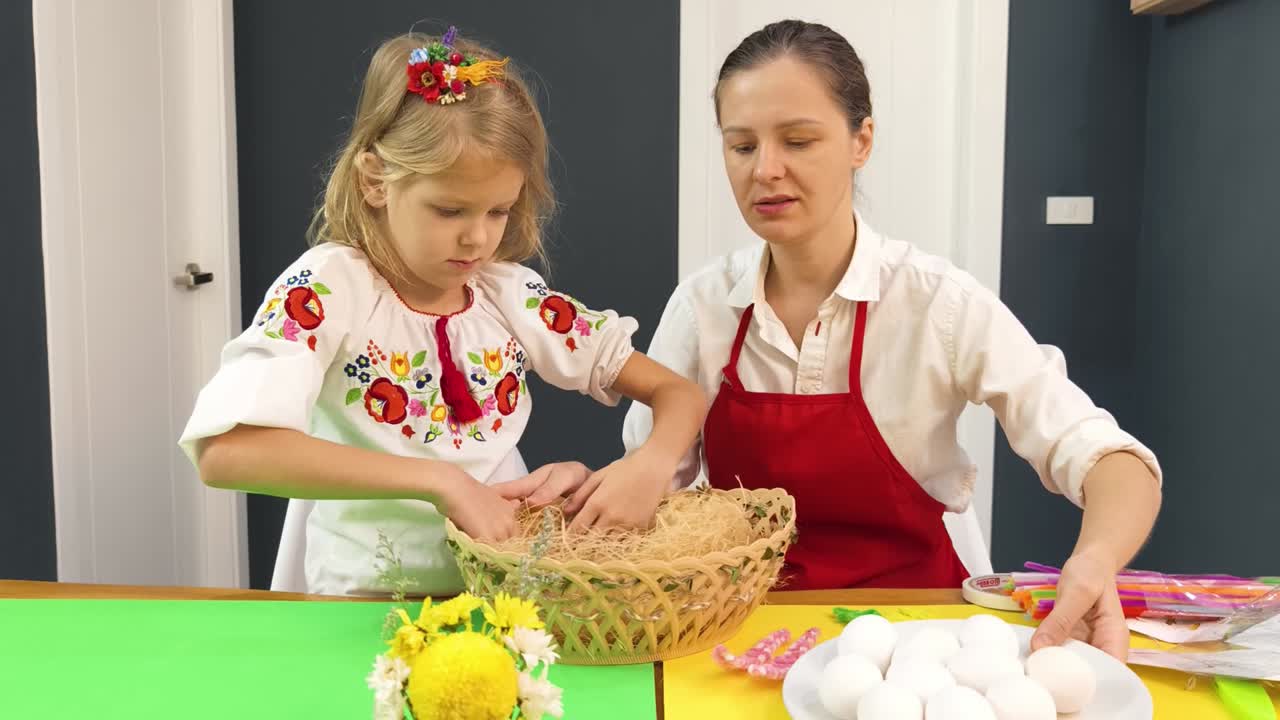 мать и дочь украшают пасхальные яйца и гнездо