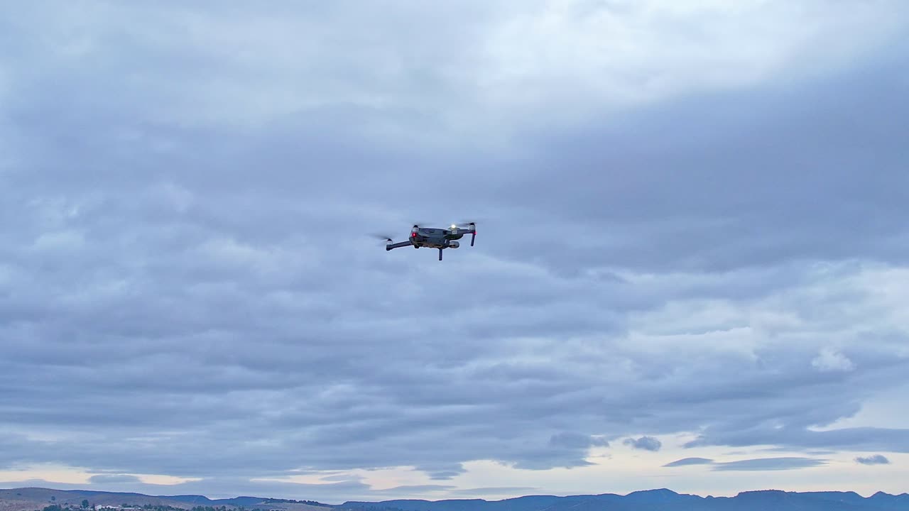 Drone in flight with position lights and signal flashes. Close aerial view. Drone flying with cloudy sky in the background.